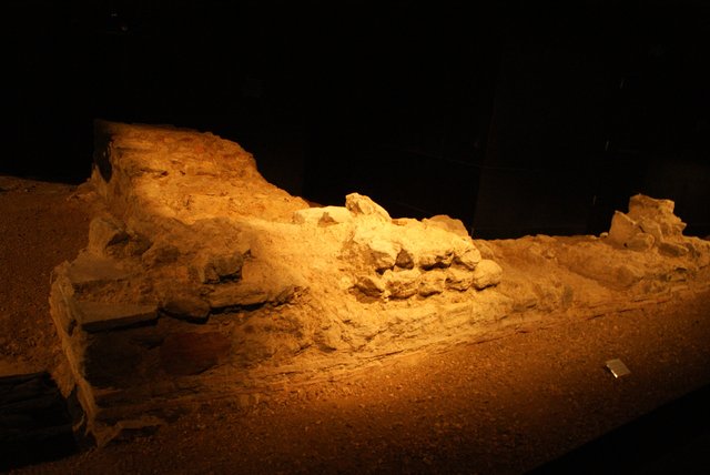 The remains of the Roman amphitheatre in the basement of the Guildhall Art Gallery, a curved wall of stone lit low in a dark room