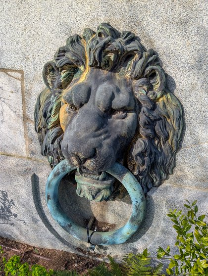 A cast lion's head on the Embankment river wall, holding a mooring ring in its mouth