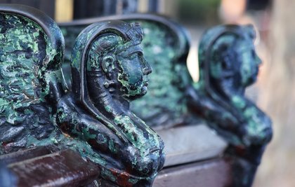 The arm rest of one of Vulliamy's Embankment benches in close-up, cast as a winged sphinx and green with patina