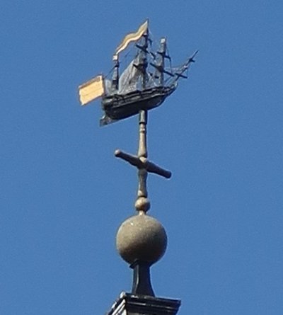 The weathervane on St Nicholas Cole Abbey: a dark three-masted ship in full rig with gilded pennants, mounted above a gilded ball and cross-vane against a clear sky